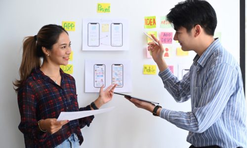 Shot of ux developer and ui designer brainstorming and discussin Shot of ux developer and ui designer brainstorming and discussing about mobile app interface wireframe design on white board.